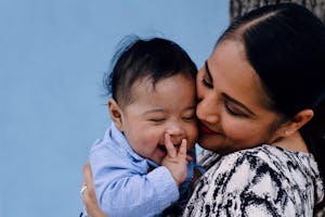 A mother affectionately embraces her baby against a serene blue background.