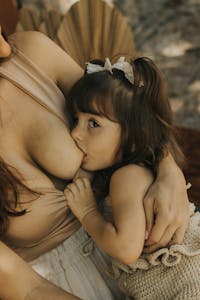 A mother breastfeeding her young child outdoors, capturing a tender bonding moment.
