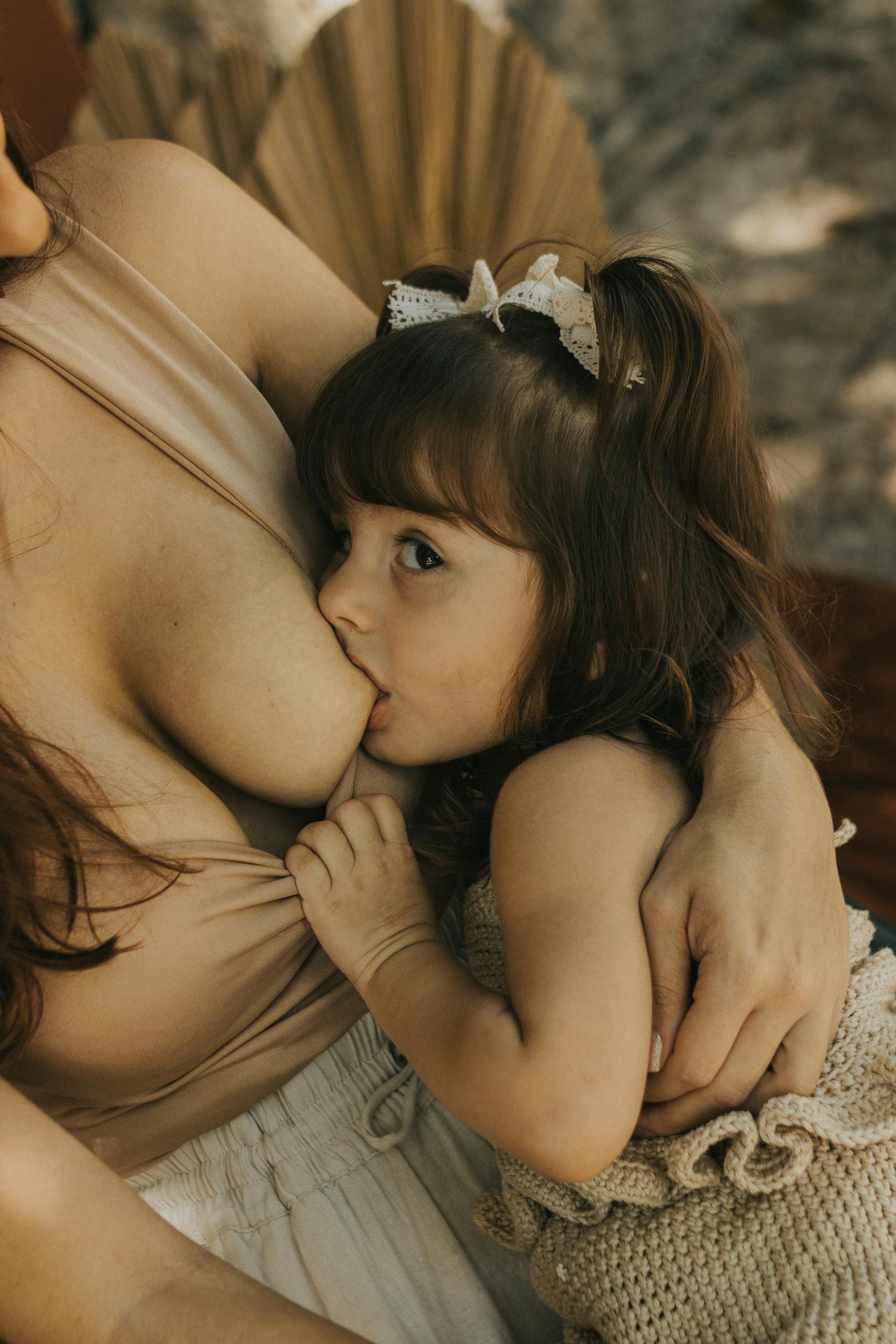 A mother breastfeeding her young child outdoors, capturing a tender bonding moment.