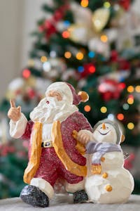 Colorful figurines of Santa and snowman with a holiday tree in the background.
