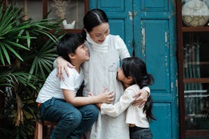 Happy smiling Asian woman with daughter and son hugging against aged building and plant on daytime
