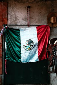 Vibrant Mexican flag displayed against a rustic wall with cowboy hat and saddle in San Salvador Cuauhtenco, Mexico.