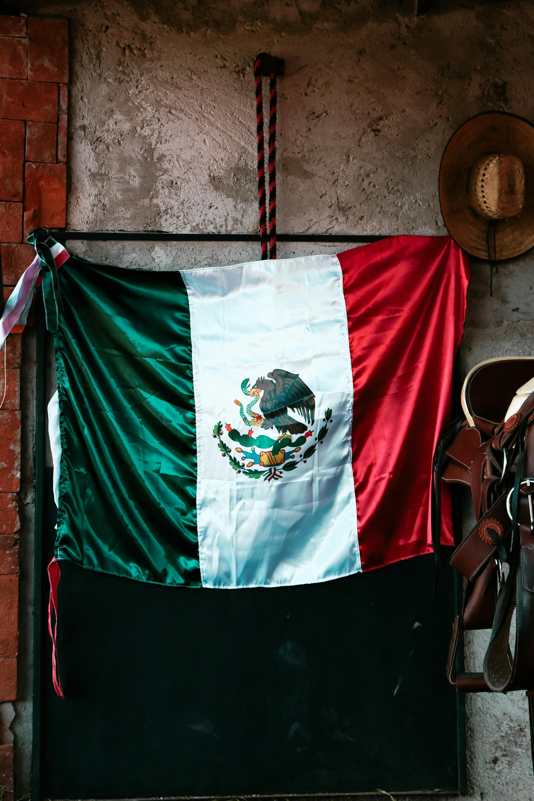 Vibrant Mexican flag displayed against a rustic wall with cowboy hat and saddle in San Salvador Cuauhtenco, Mexico.